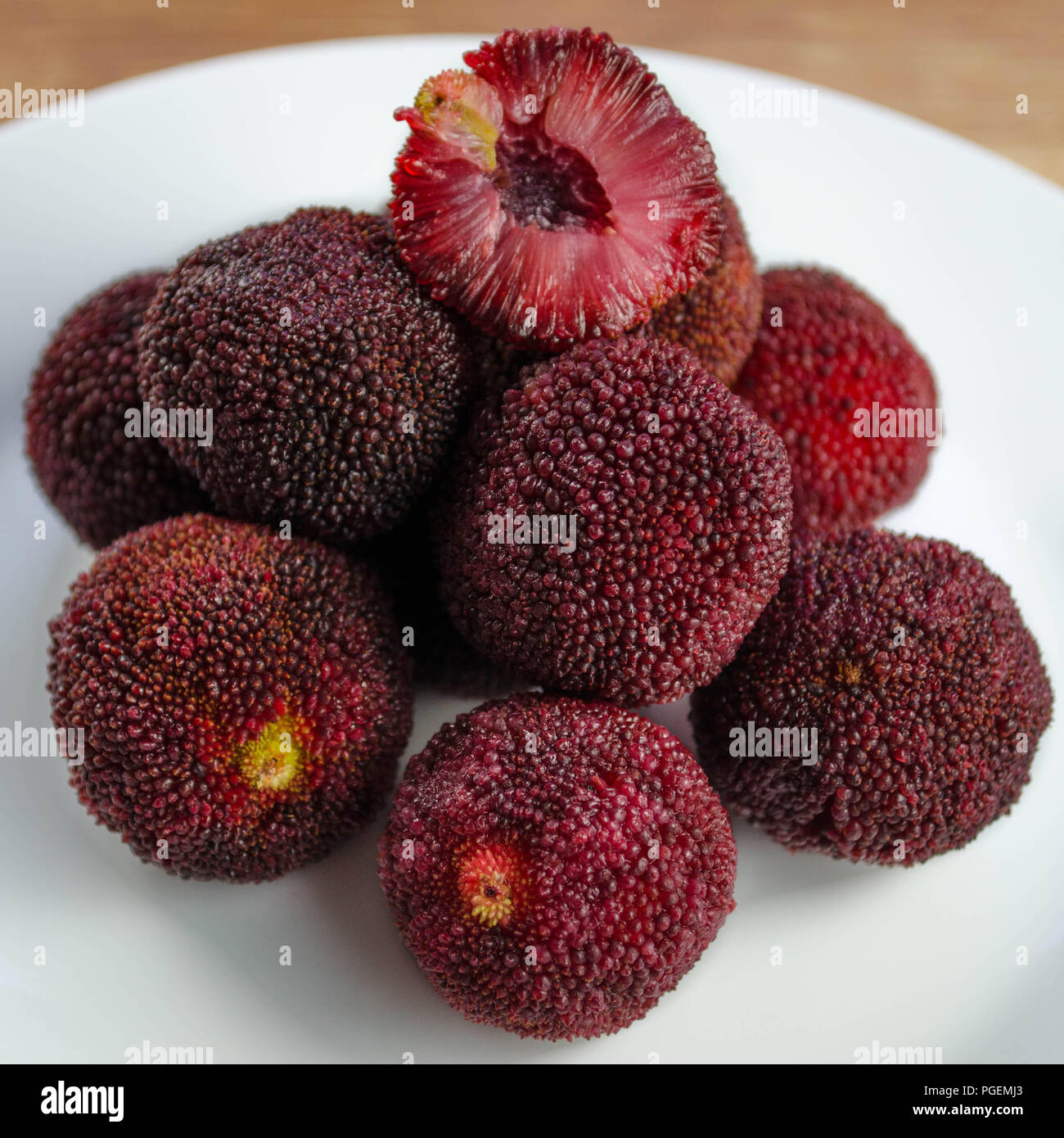 Chinese bayberries (Myrica rubra), aka yangmei, waxberry, or yamamomo.  Whole fruits and one cross-sectioned fruit are shown on a white plate. Stock Photo