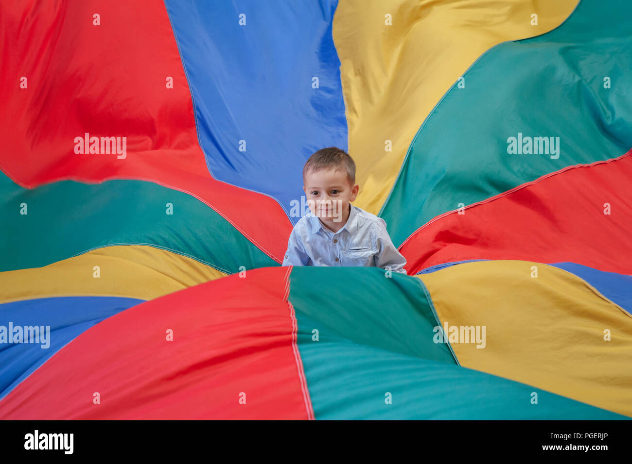 Portrait of white Caucasian child boy toddler sitting in the center of playground rainbow parachute celebrating his birthday at party Stock Photo