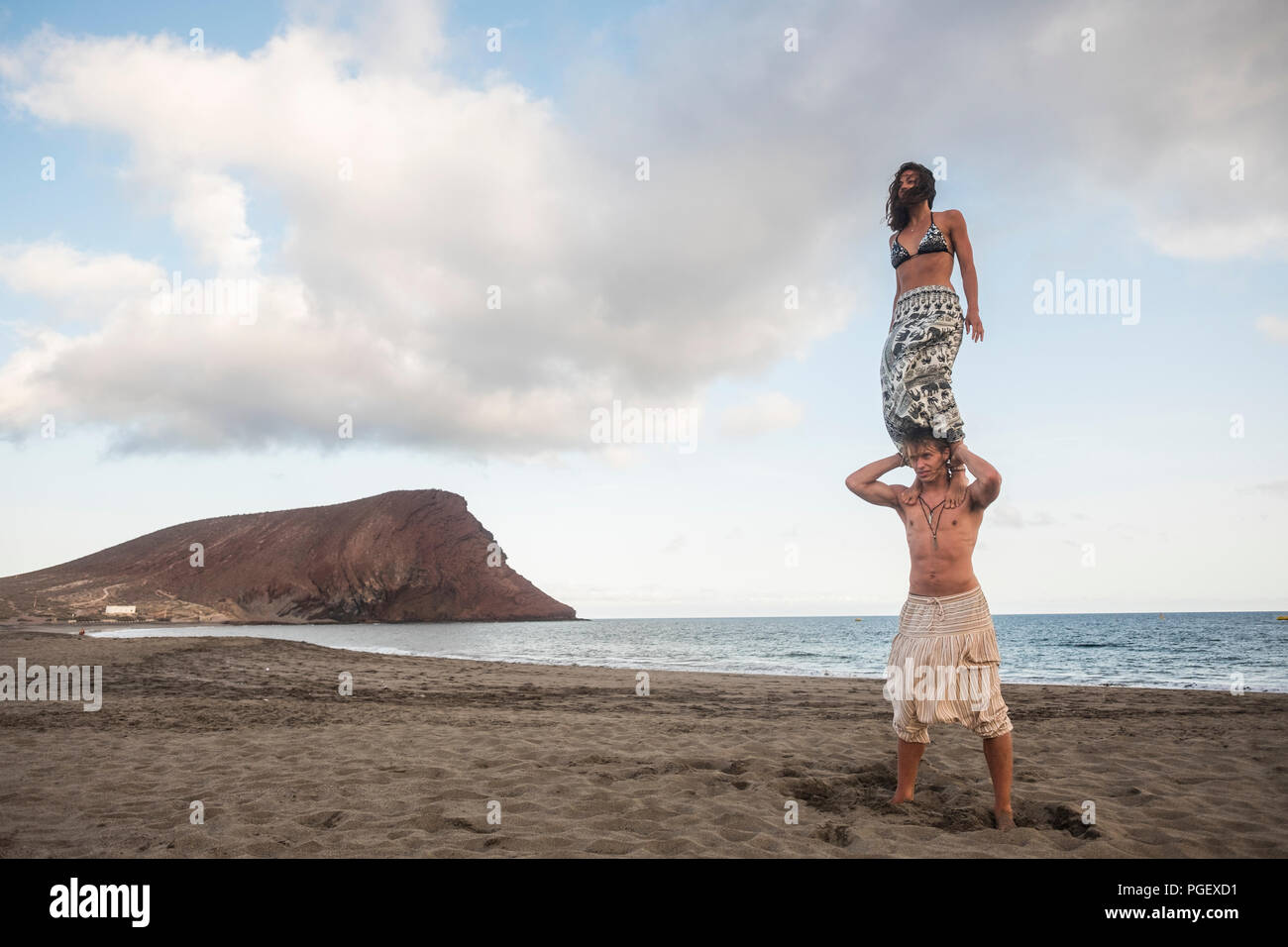 acrobatic balnced position for beautiful brave couple man and woman young people standing one up the other at the beach with ocean in background. extr Stock Photo