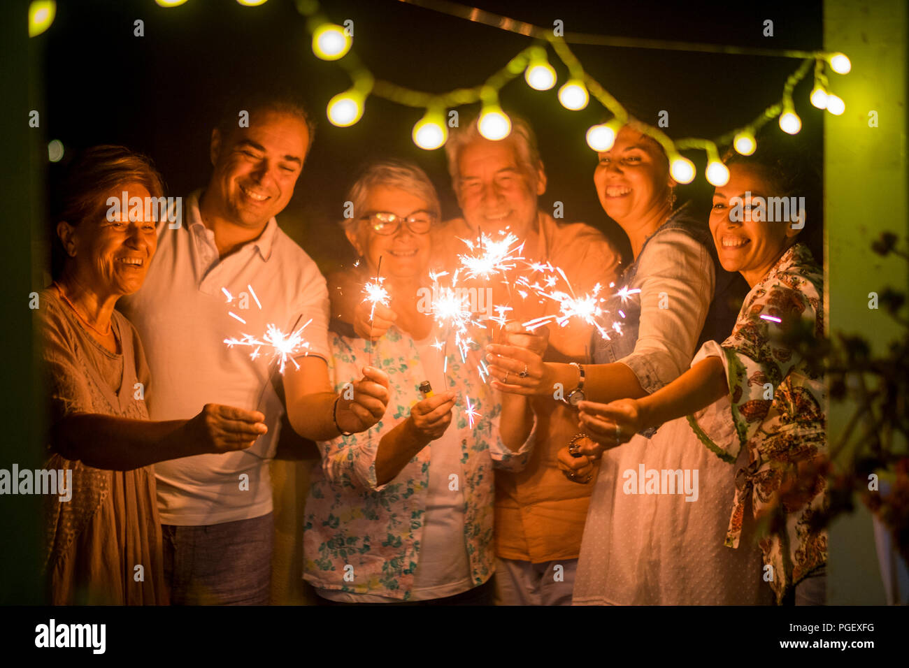 group of people celebrate an event like new years eve or birthday all together with sparkles light by night in the dark. smiles and having fun in frie Stock Photo