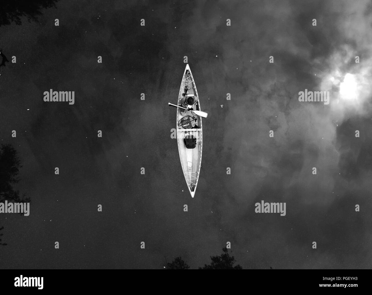 drone shot looking down on a man in a canadian canoe floating on a river in black and white Stock Photo