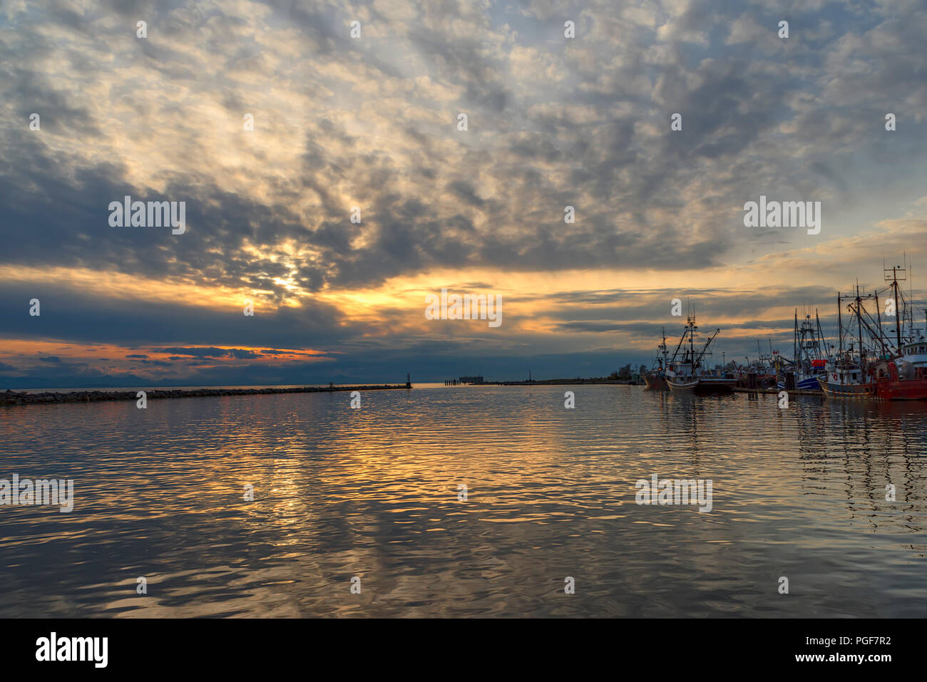 fishing boats and boats are on the pier at the end of the day in the bay. The sun shines behind the clouds and the radiance reflects in the waves of t Stock Photo