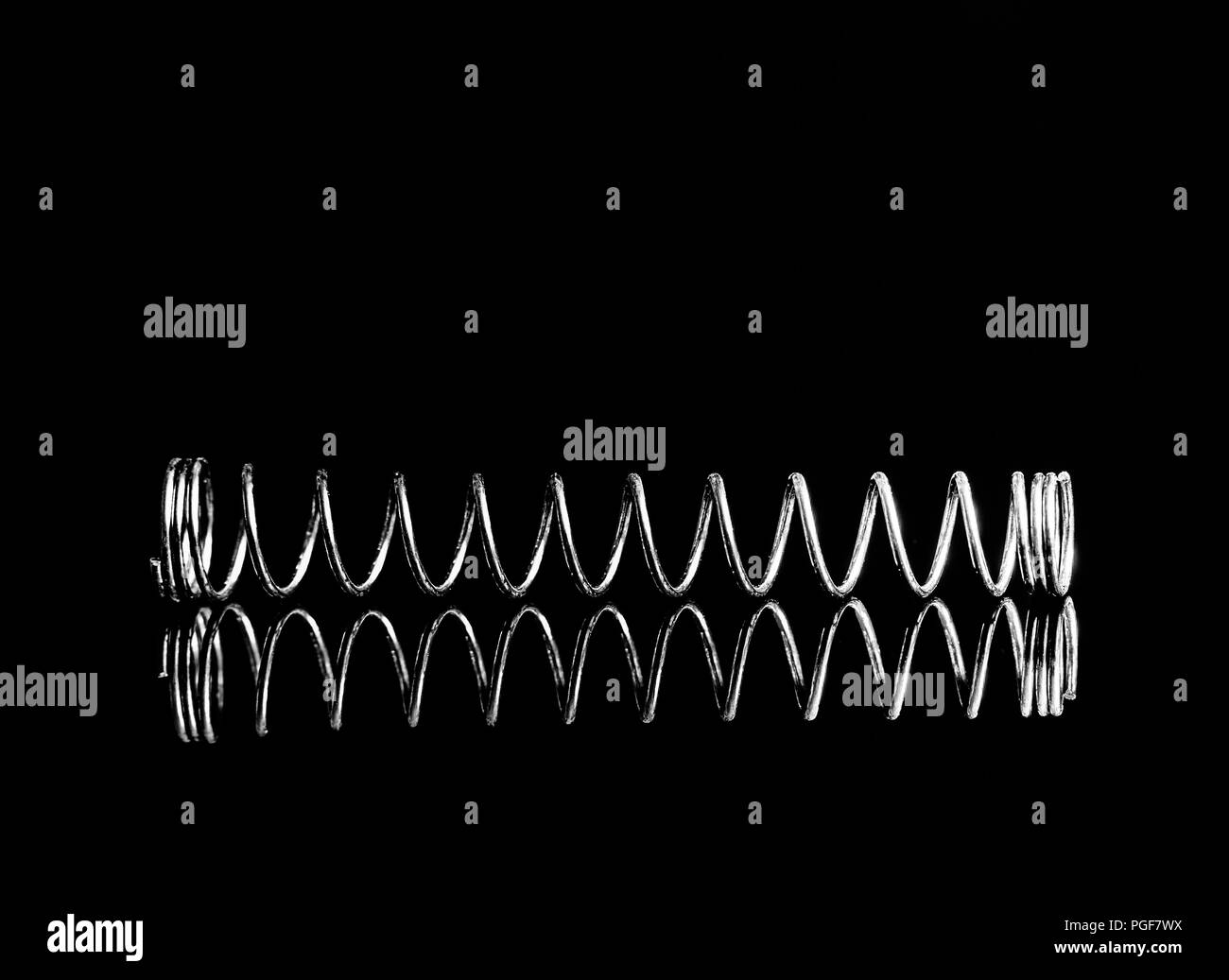 Silver metal spring isolated on black background with reflection. Macro photography Stock Photo