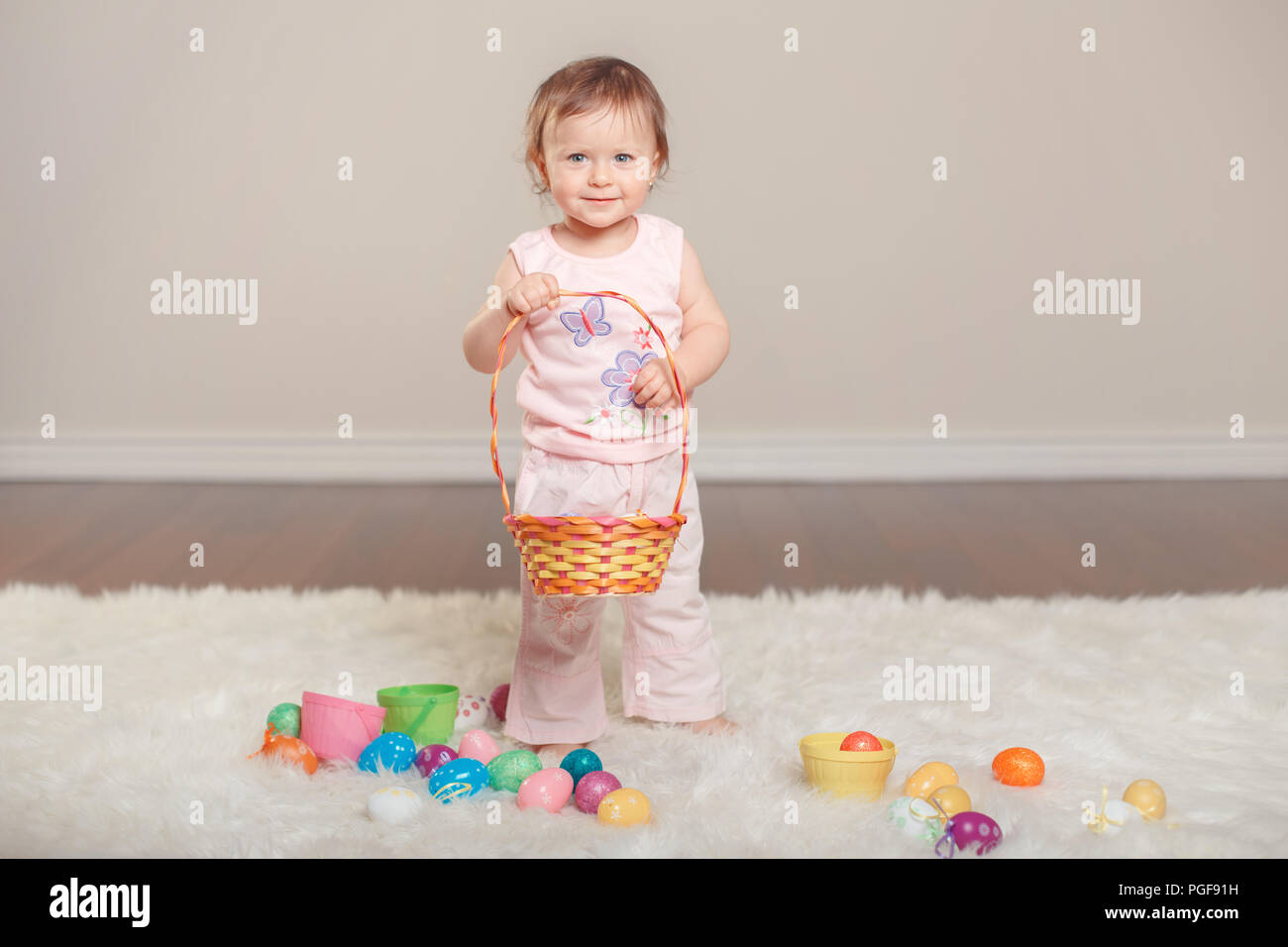 Cute adorable Caucasian baby girl in pink shirt and pants celebrating traditional Easter Christian holiday. Kid child holding basket and playing with  Stock Photo