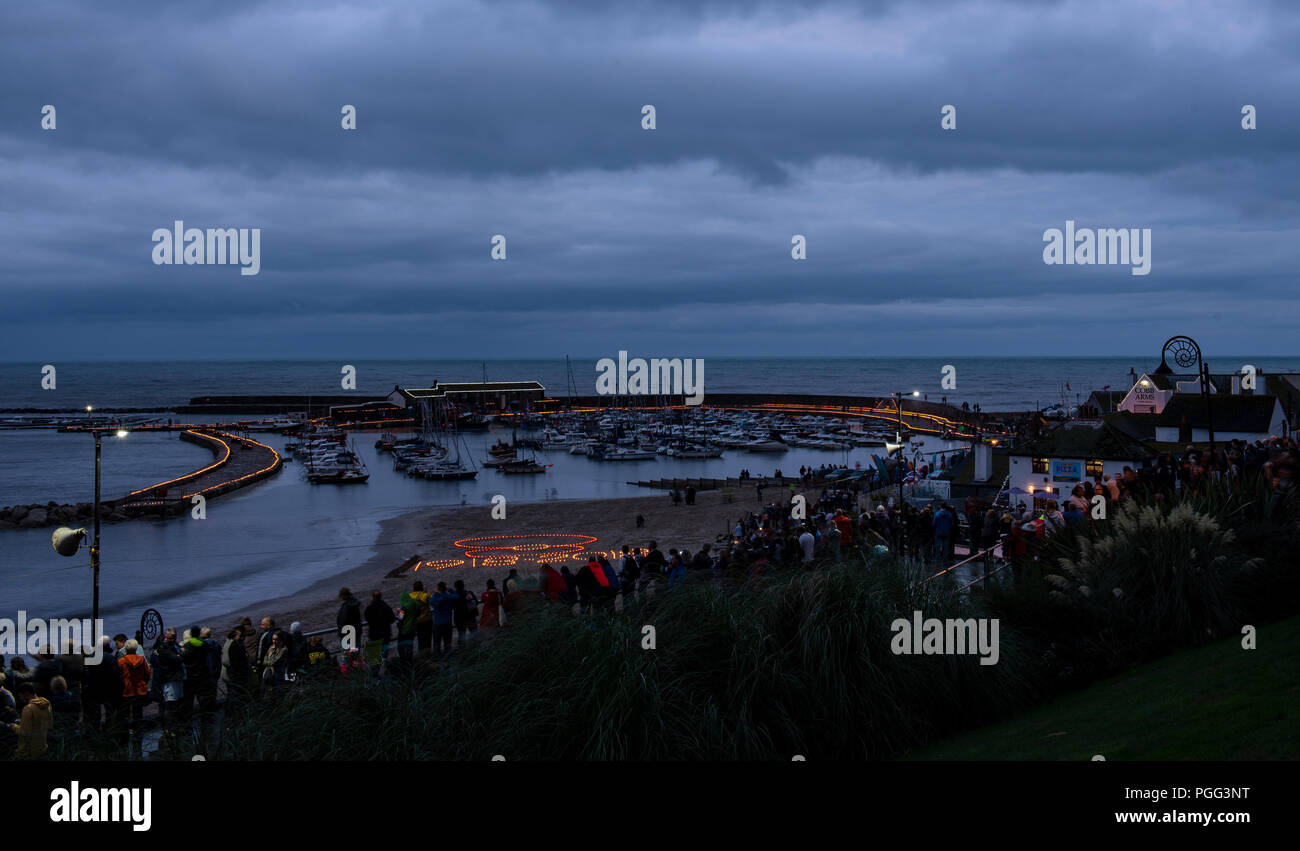 Lyme Regis, Dorset, UK. 20th August 2018. UK Weather: Crowds gather at Lyme Regis on a cloudy and wet evening to witness the lighting of over 4000 candles along the iconic Cobb at dusk.  The event, organised by the Rotary Club this year also commemorates the centenery of the ending of the First World War with the event raising money for the British Legion and local charities. Credit: PQ Images/Alamy Live News. Stock Photo