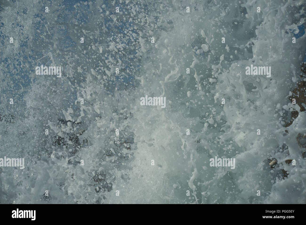 Water droplets suspended in the air as a wave hits a sea wall. Large splash of foaming spray. Stock Photo