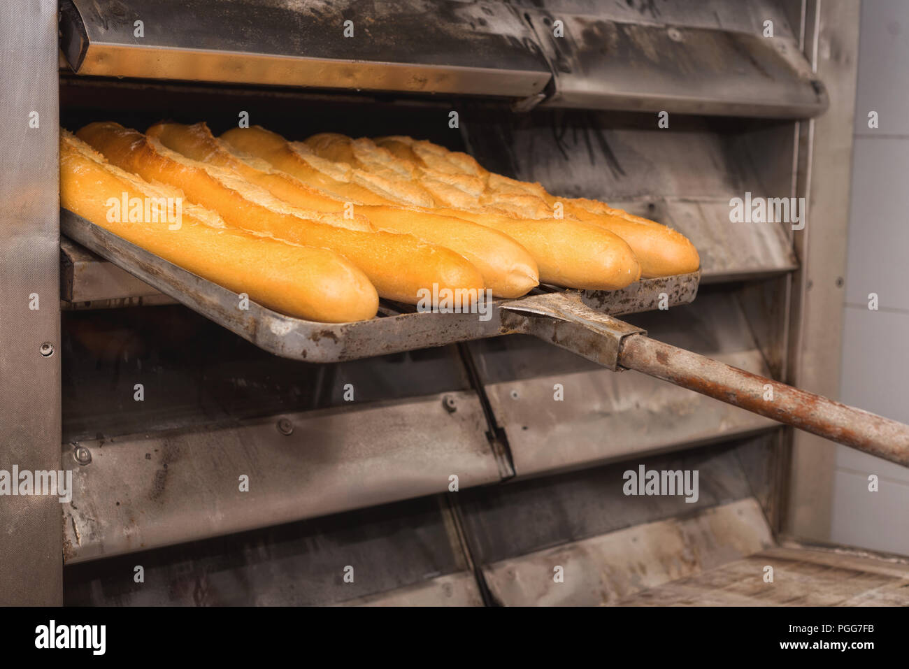 Baker taking out freshly baked bread from the oven of a bakery stock photo