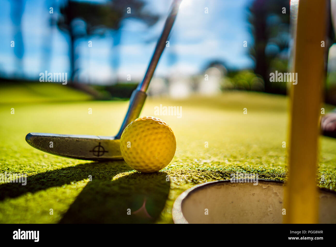 Mini Golf yellow ball with a bat near the hole at sunset Stock Photo