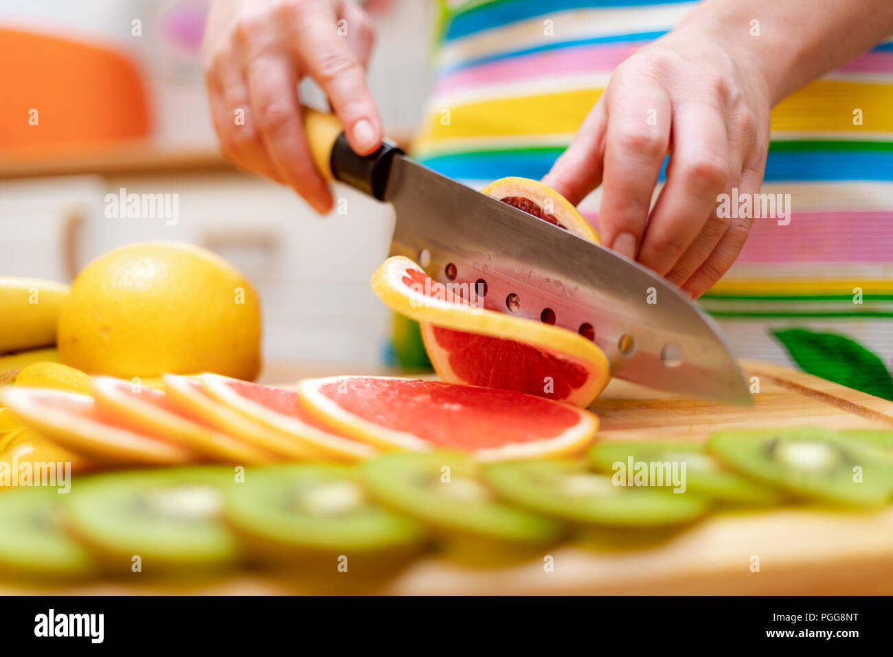 Women's hands Housewives cut with a knife fresh grapefruit on the cutting Board of the kitchen table Stock Photo
