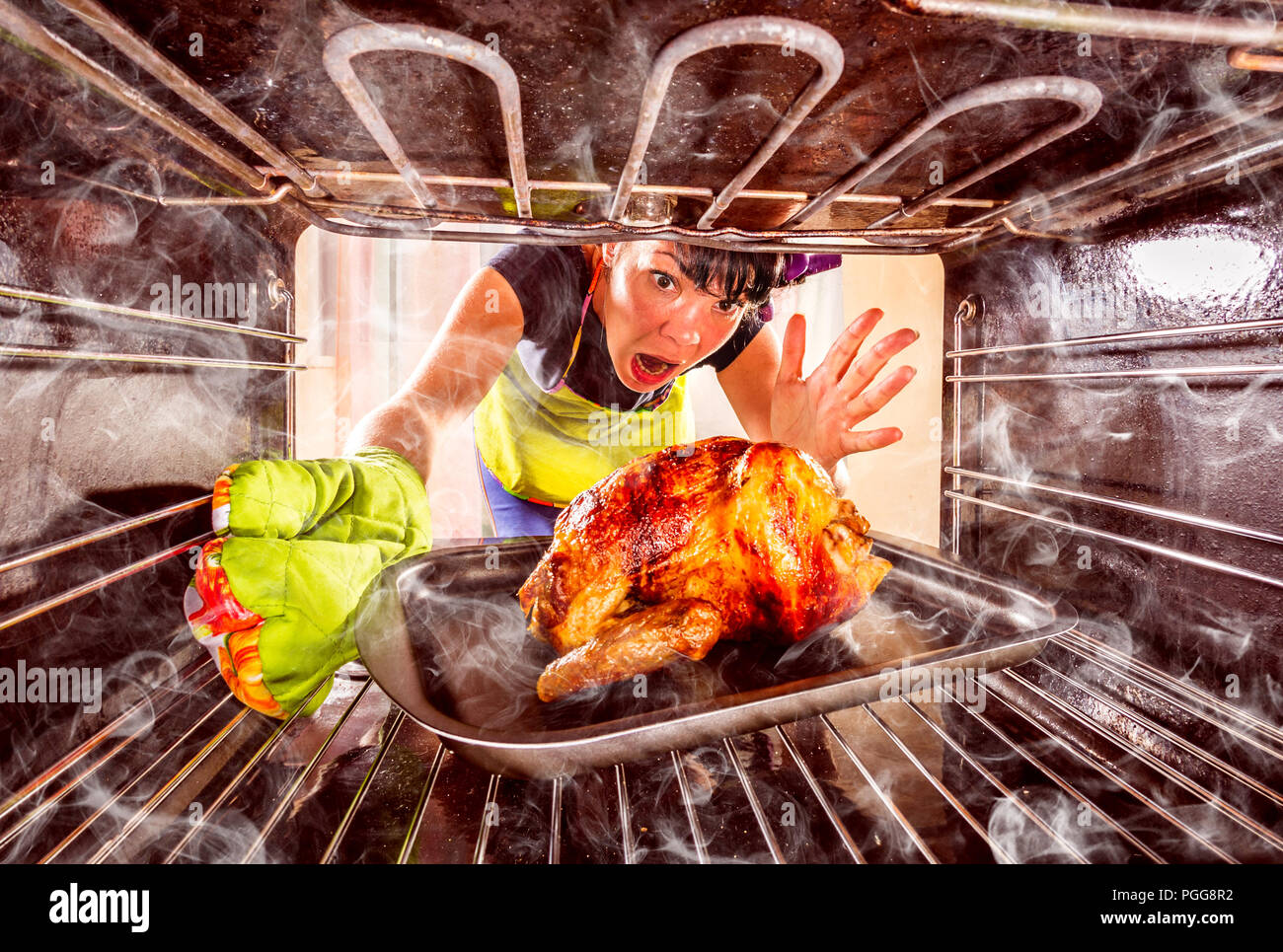 Funny Housewife overlooked roast chicken in the oven, so she had scorched (focus on chicken), view from the inside of the oven. Housewife perplexed an Stock Photo