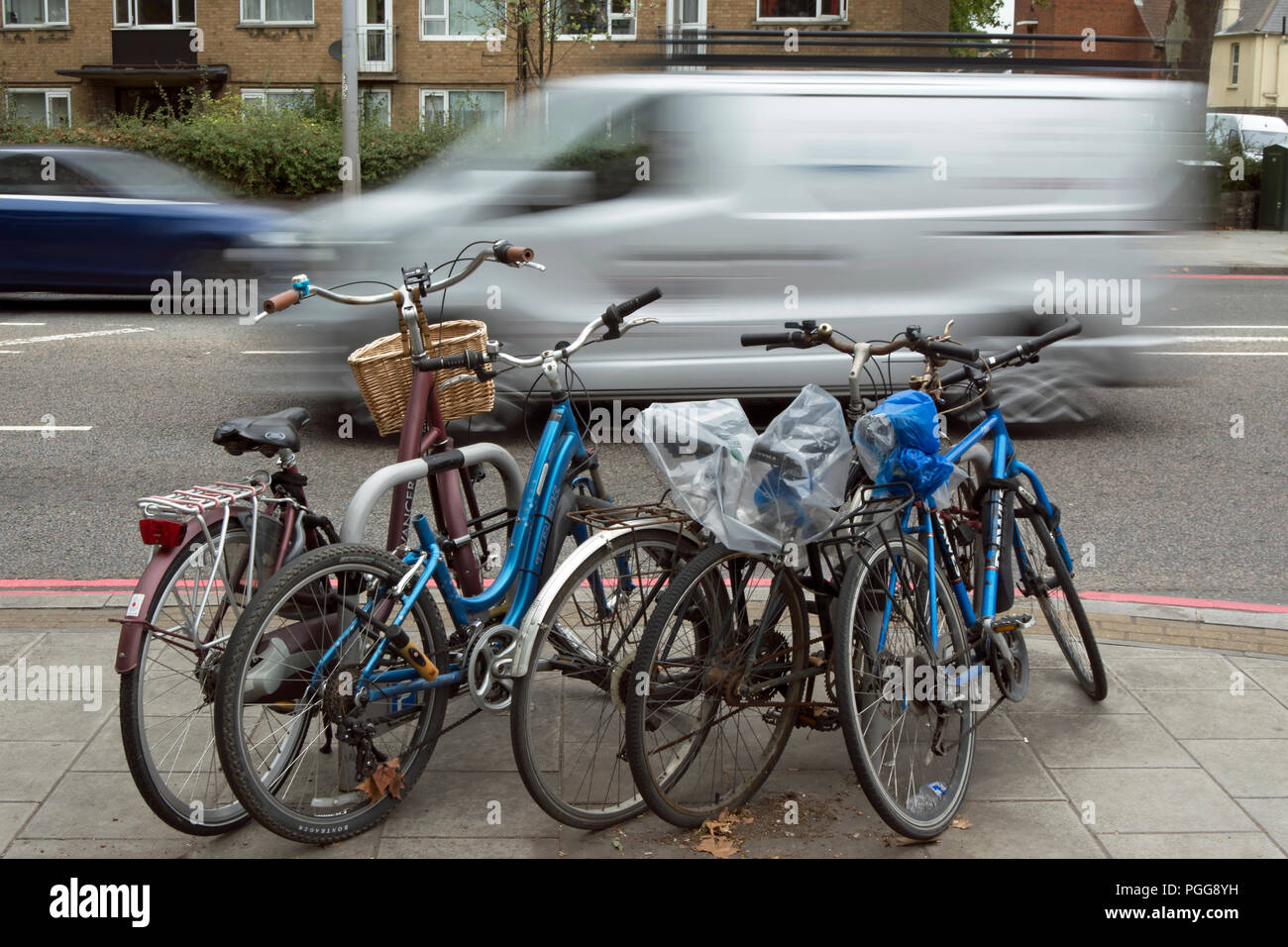 white van seen in blurred motion passes a rack of parked bicycles, in east sheen, london, england Stock Photo