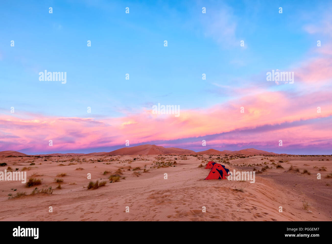 Camping in the Sahara Desert in Morocco. A row of little red tents under a colorful sunrise. Adventure travel theme. Stock Photo