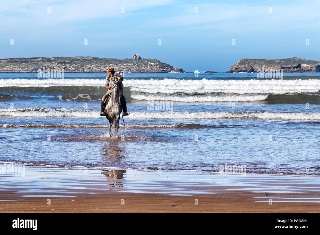 ESSAOUIRA, MOROCCO-DEC 22, 2012: Man riding a horse in the ocean waves at Essaouira, Morocco. Horseback riding is a popular activity on the beach, bot Stock Photo