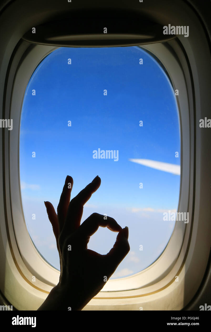 Silhouette of female's hand posing OK sign against airplane window with
