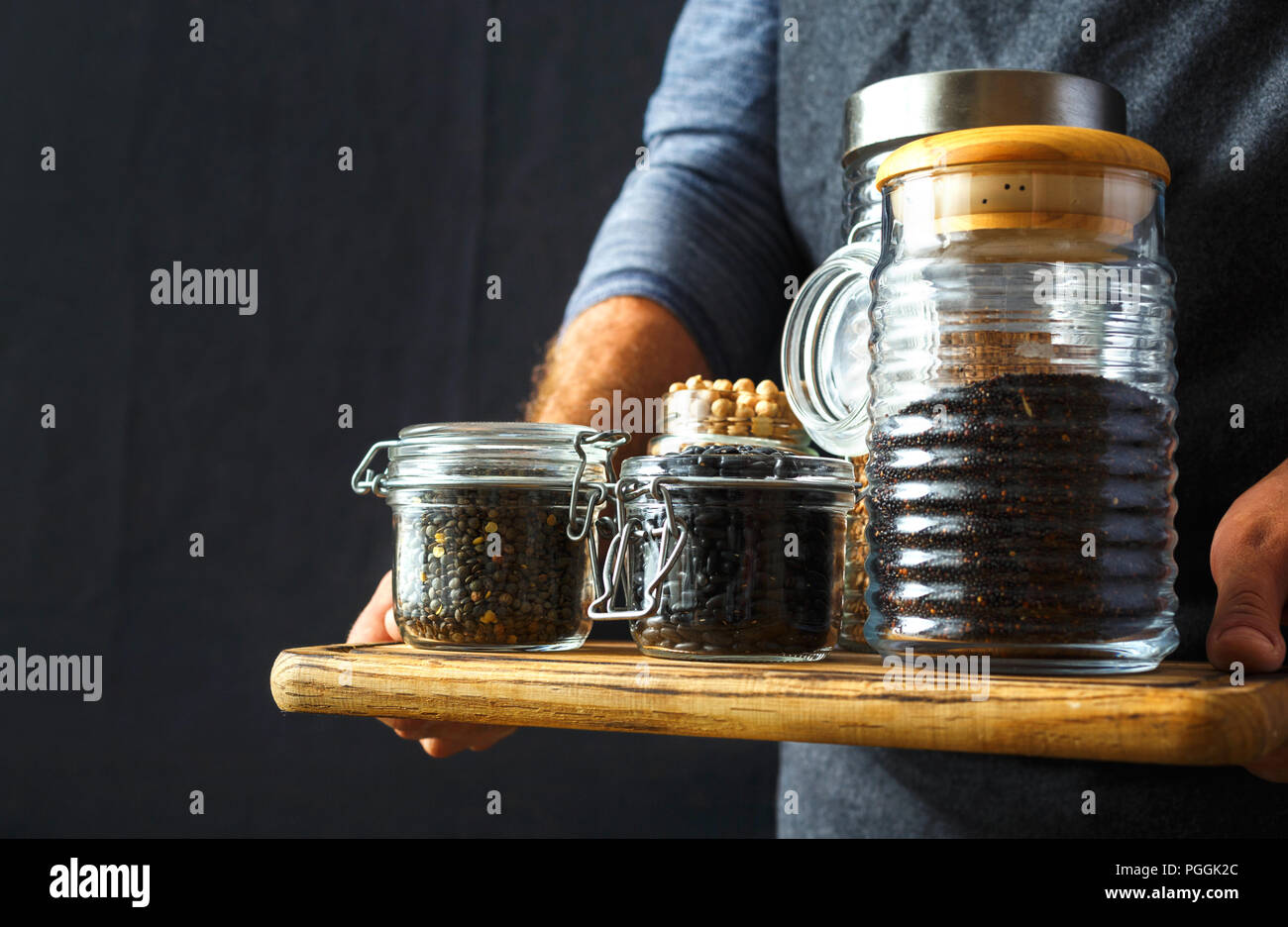 Set groats in glass jars in hands man: black quinoa, chickpeas, black beans, green lentils, buckwheat dark background healthy vegan food concept Stock Photo