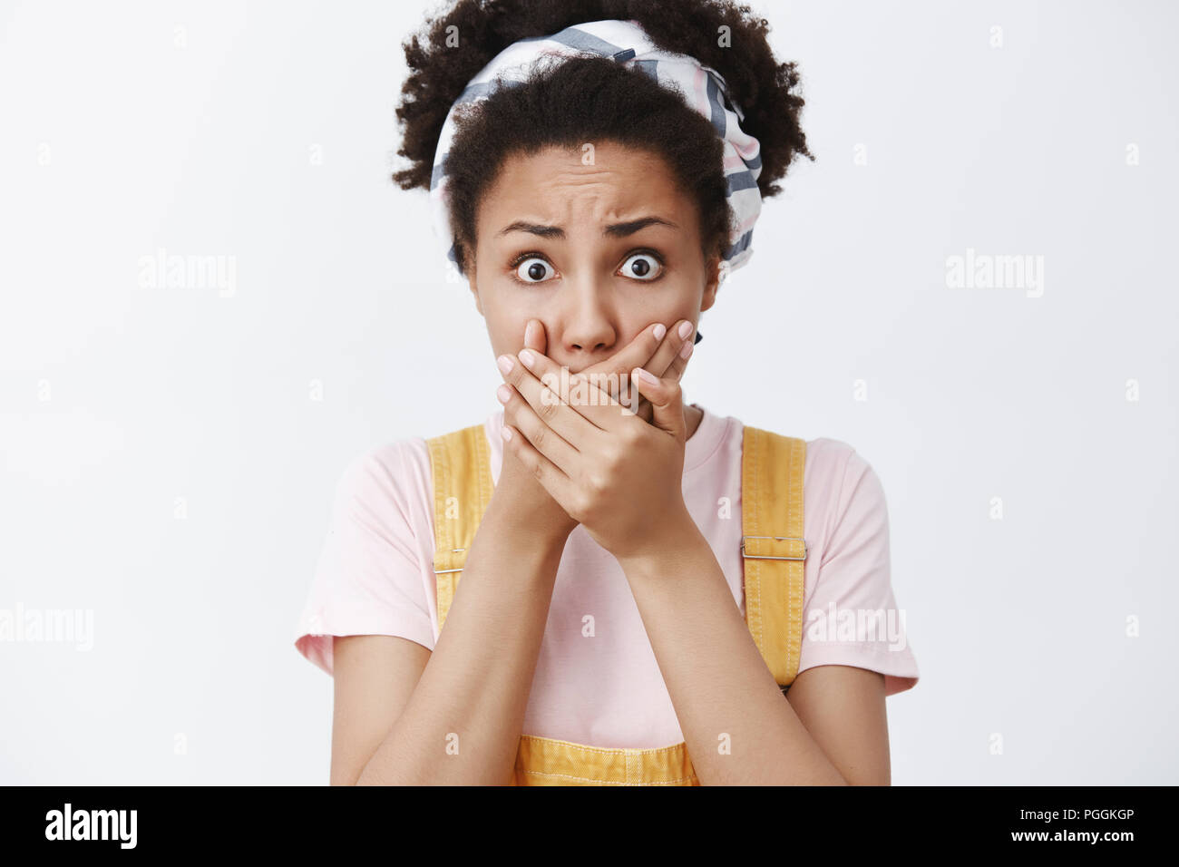 Woman heard shocking news being speechless and stunned, covering mouth with both palms from upset and shook, staring and frowning at camera, terrifying with accident over gray background Stock Photo