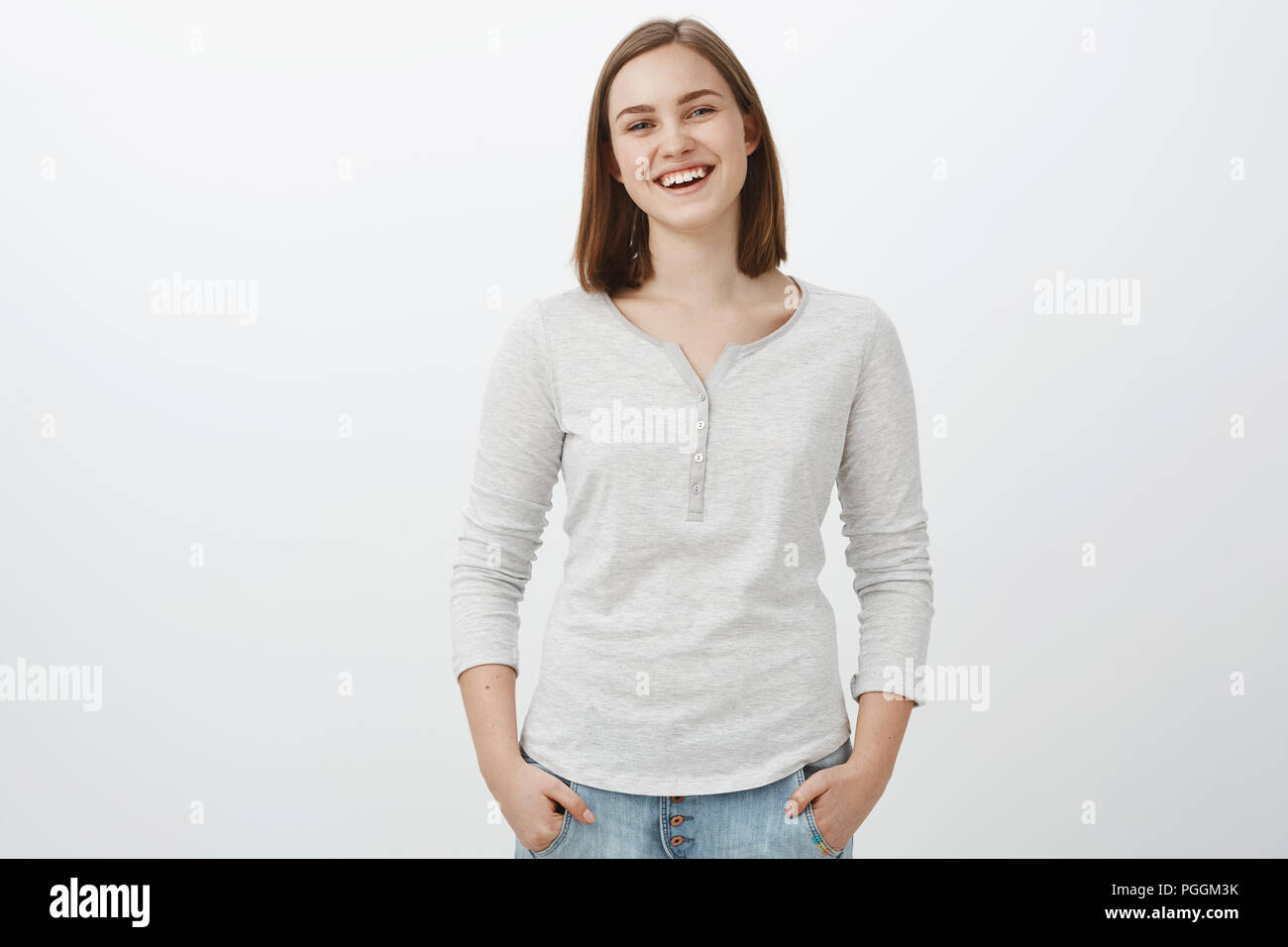 Girl feeling happy being teenager and living carefree life. Portrait of sociable friendly-looking charming female brunette holding hands in pockets casually and smiling joyfully at camera Stock Photo
