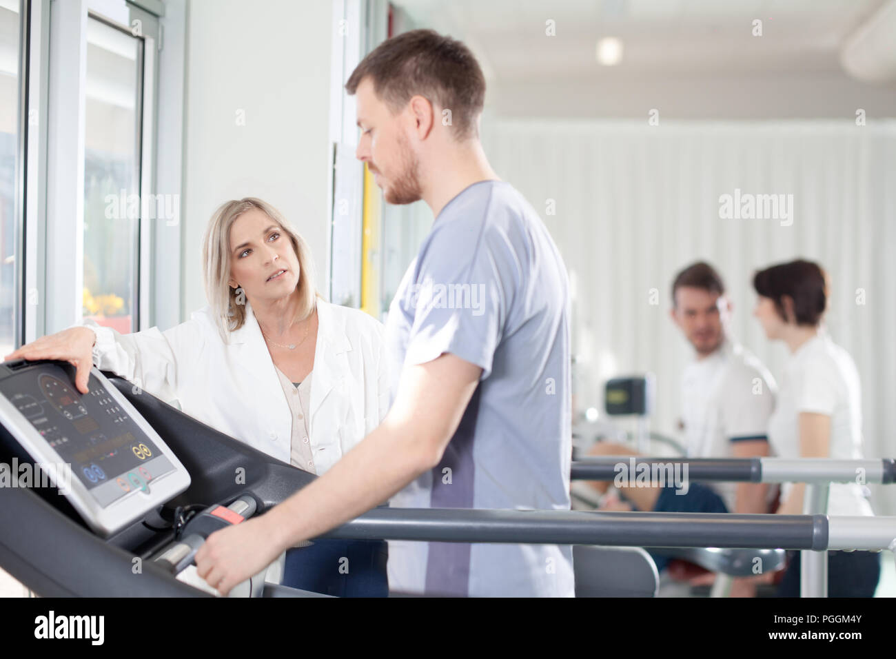 athlete on the treadmill he performs the instructions of physical therapist who assists him. in the background other athletes Stock Photo