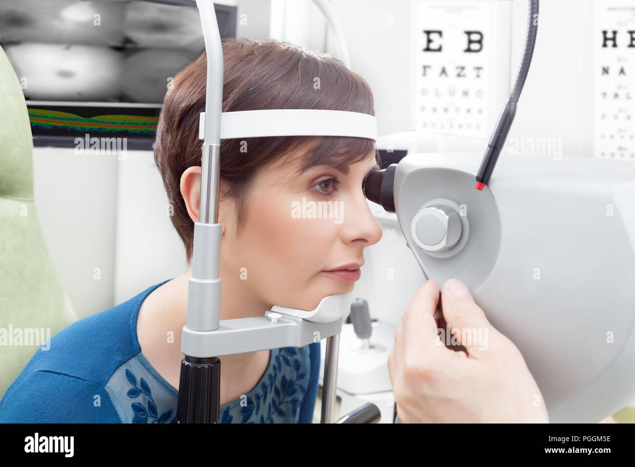Woman with short haircut close-up from her side having eye examination at ophthalmology room in hospital, male oculist hand adjusting the device in fo Stock Photo