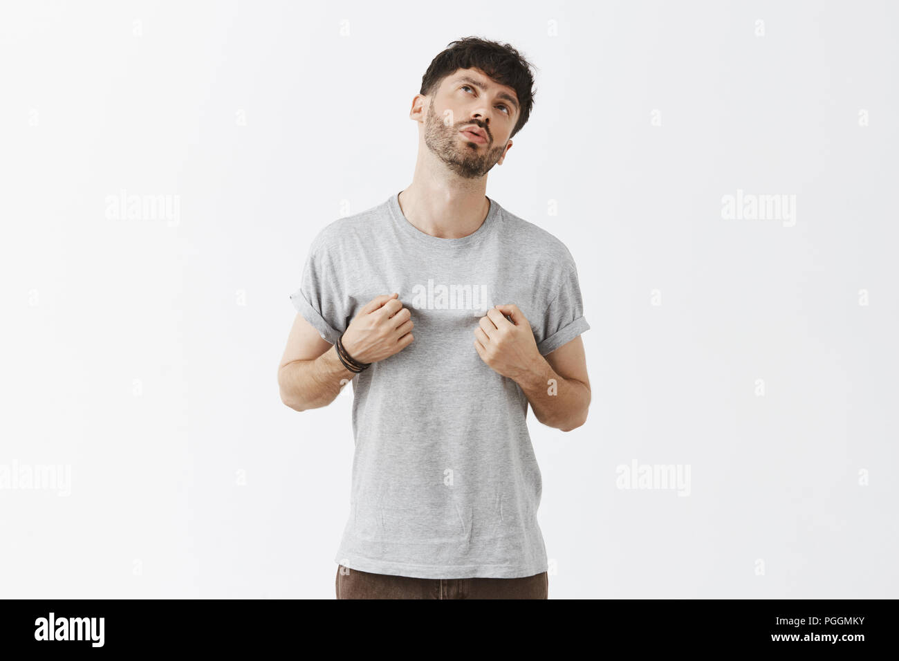 Displeased and picky stylish guy expressing dislike being displeased with new t-shirt girlfriend bought touching shirt as if feeling hot breathing out and looking up with tired expression Stock Photo