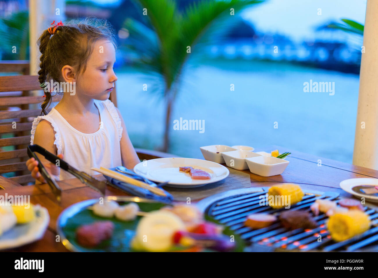 Cute little girl having dinner at outdoor restaurant on summer day Stock Photo