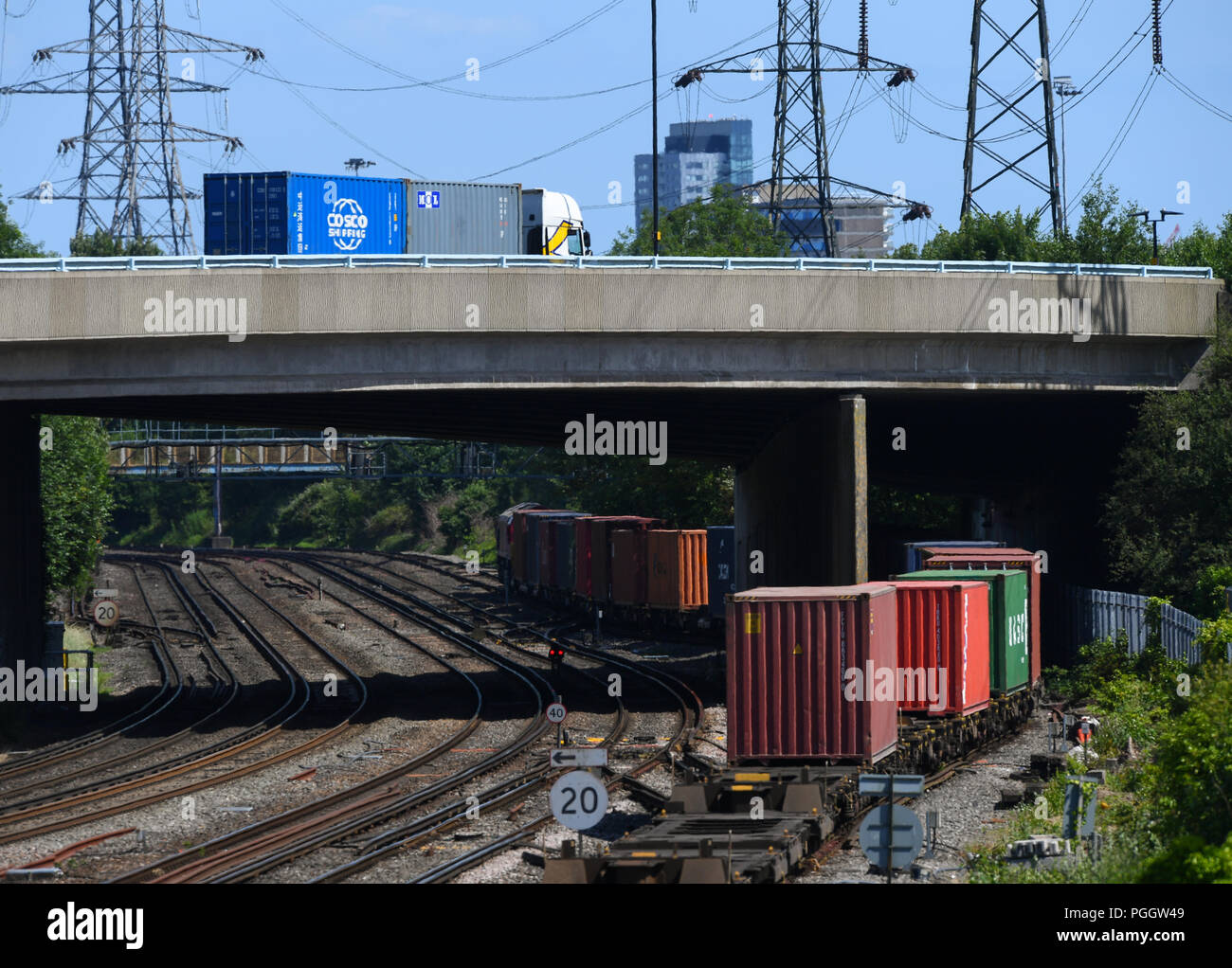 Road versus rail, a truck carrying containers passes above a container train below. Stock Photo