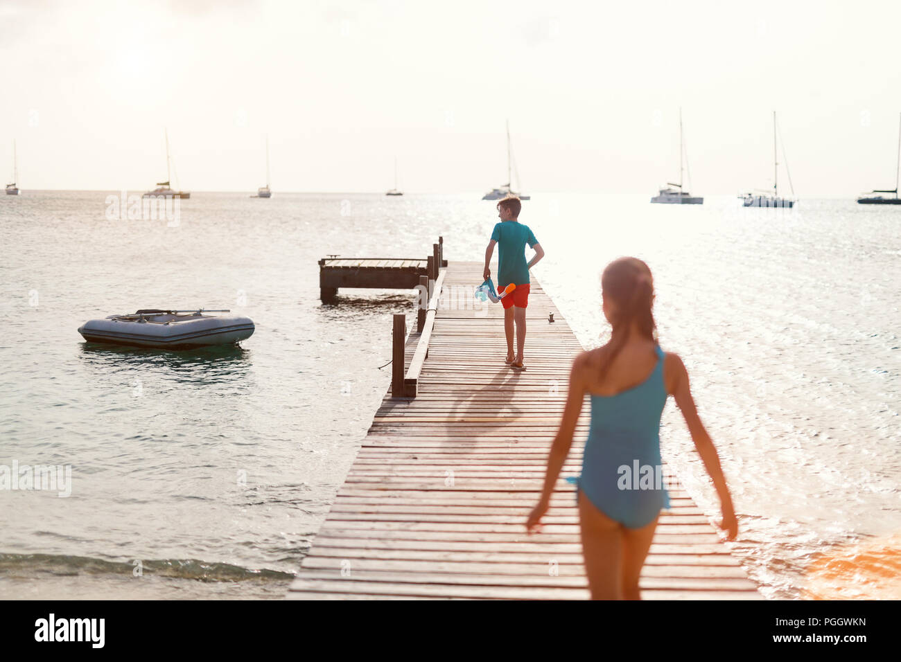 Back view of kids brother and sister on a wooden dock at sunset walking towards sea Stock Photo