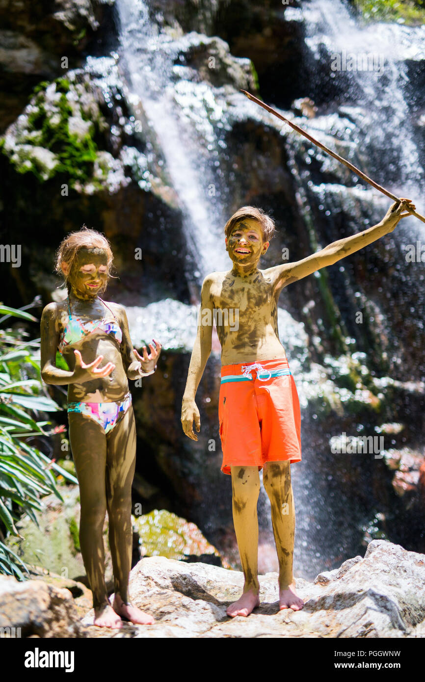 Kids brother and sister covered in mud in front of beautiful waterfall traditional tourist activity on St Lucia island in Caribbean Stock Photo