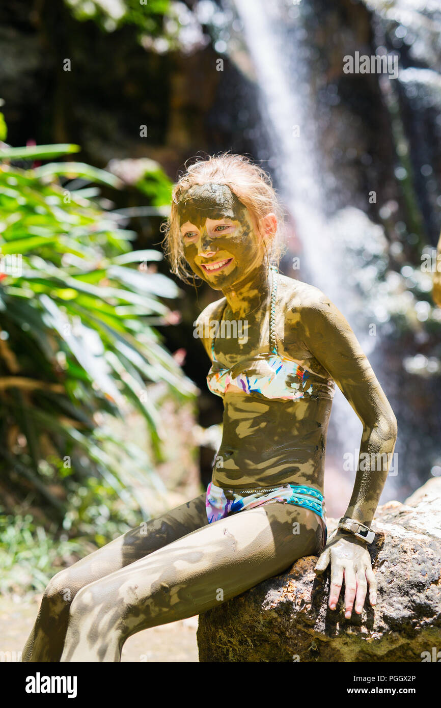 Portrait of cute little girl covered in mud in front of beautiful waterfall traditional tourist activity on St Lucia island in Caribbean Stock Photo