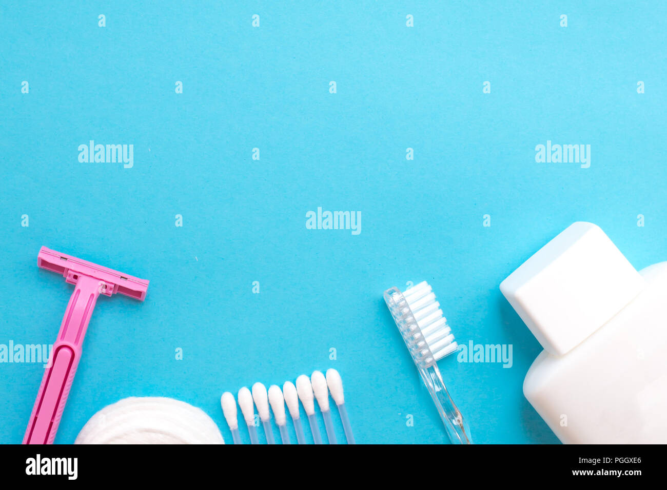 top view personal care products. white bottle, pink razor, ear sticks, cotton pads, toothbrush on blue background. copy space Stock Photo