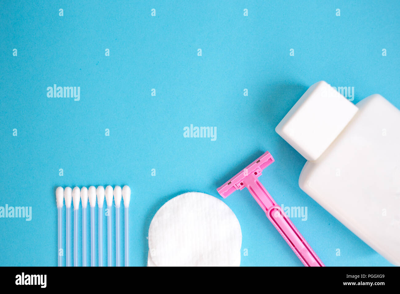top view personal care products. white bottle, pink razor, ear sticks, cotton pads, toothbrush on blue background. copy space Stock Photo
