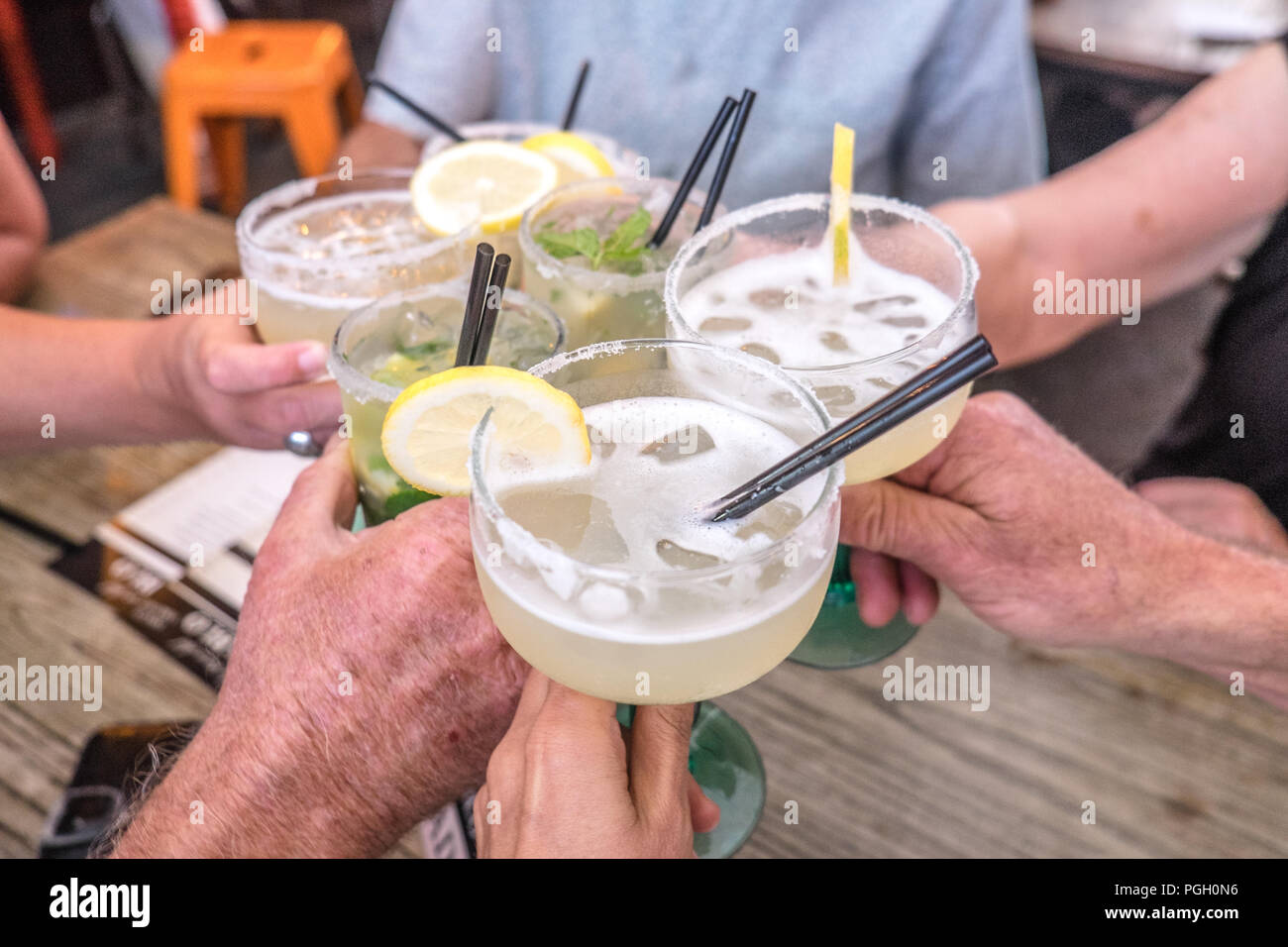 Hands young and old celebrating making a toast and clinking cocktail glasses with margaritas and mojito alcoholic drinks at celebration Stock Photo