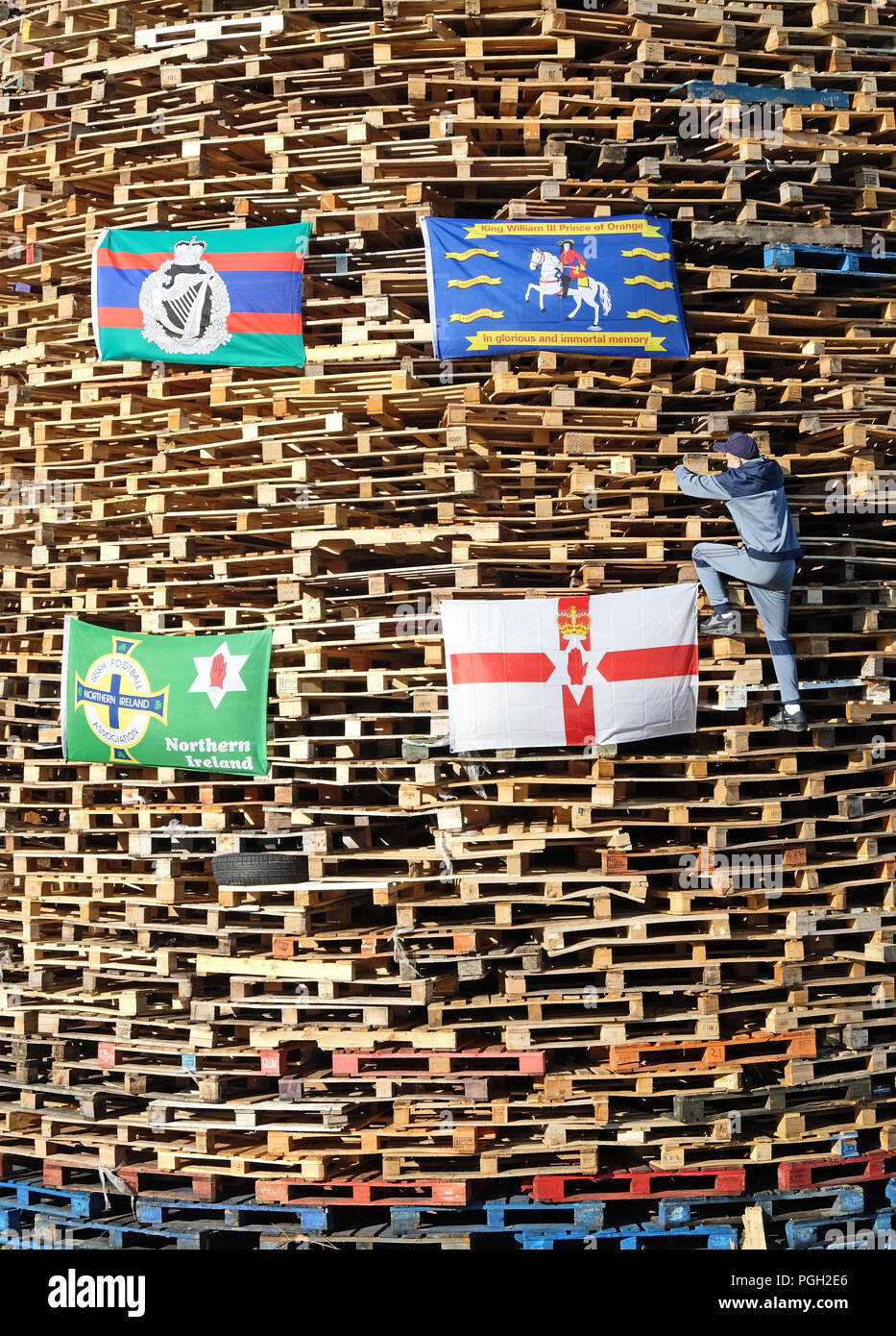 Young man climbing 12th bonfire made with pallets, Larne, Northern Ireland. Stock Photo