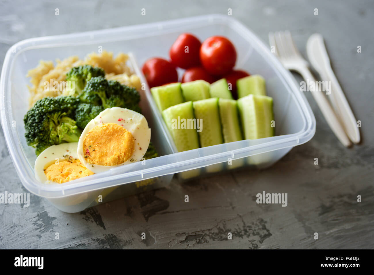 Lunch box with healthy food. Rice, broccoli, tomato, cucumber, eggs, apple and water. On grey concrete background Stock Photo