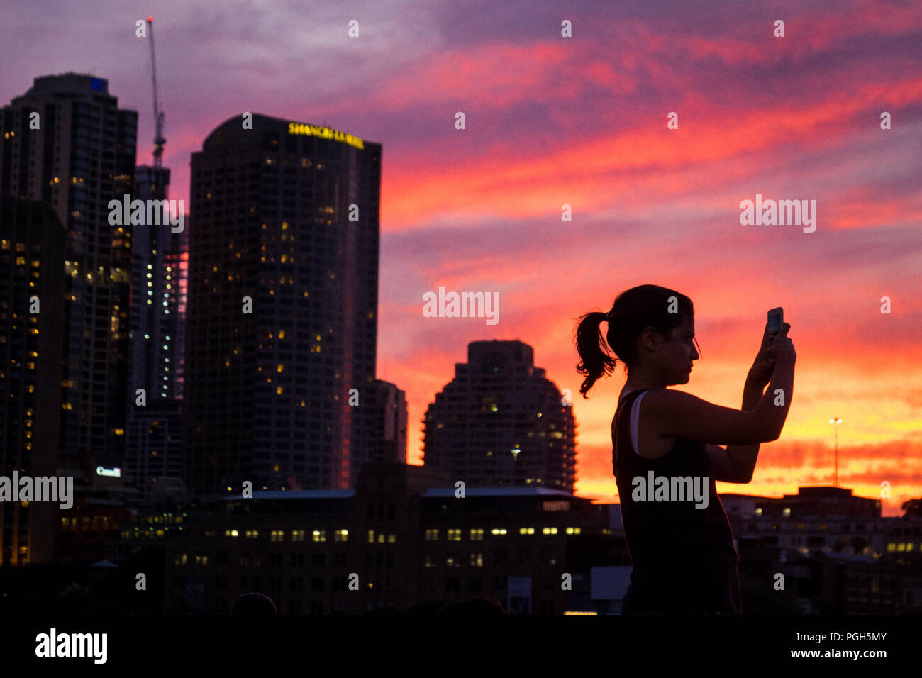 A woman taking a panoramic photo on her smartphone of the sunset over Sydney harbour bridge, Australia Stock Photo