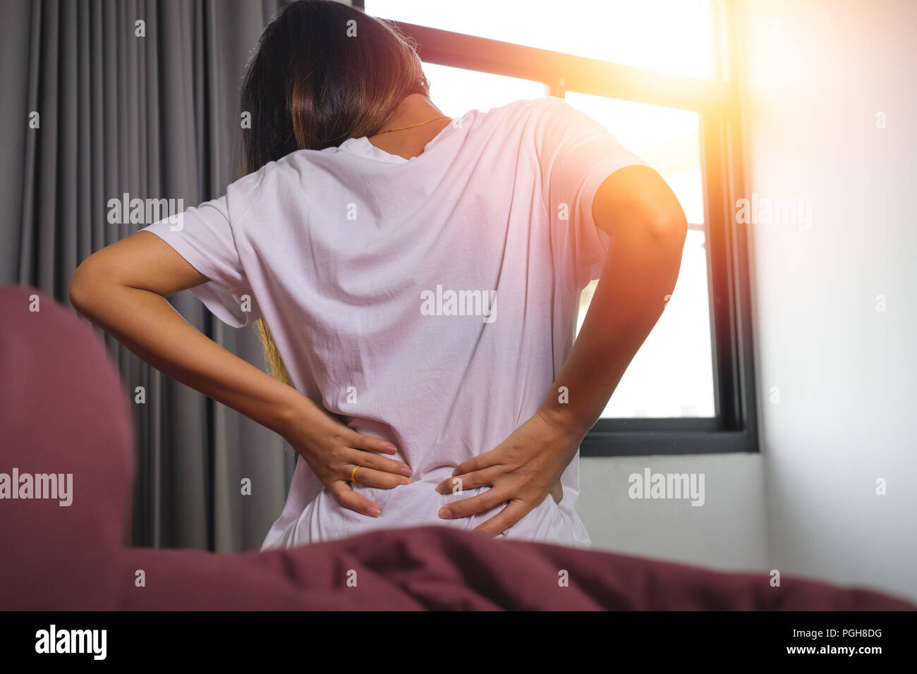 Young woman with back ache, she is sitting on the bed and touching her
