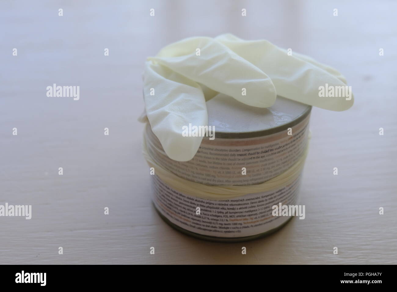 A sterile latex glove being used as an alternative to cling film to cover tin of food Stock Photo