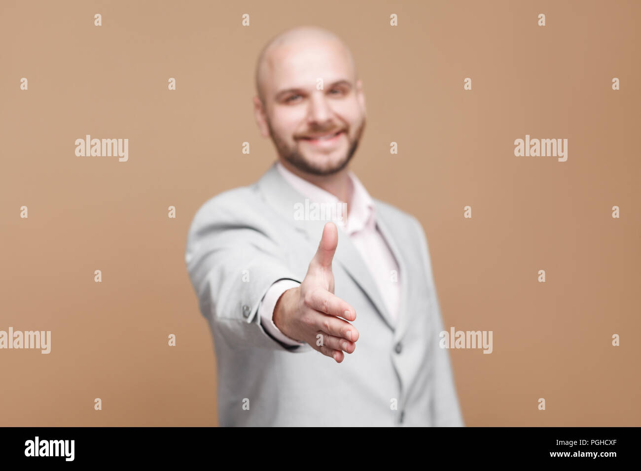 Nice to meet you. happy toothy smiling handsome middle aged bald bearded businessman in classic gray suit standing and giving handshake. indoor studio Stock Photo