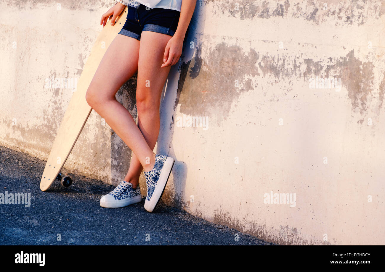 Bare legs of skater girl in short shorts leaning back used wall with her  longboard near with her legs crossed a lot of space for text Stock Photo -  Alamy