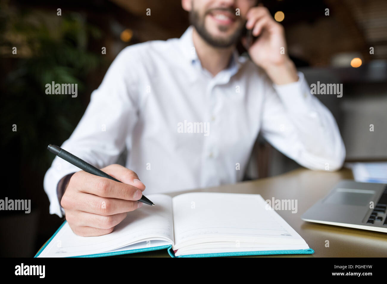 Close up of male hand holding pen over open notebook while working in cafe, copy space Stock Photo