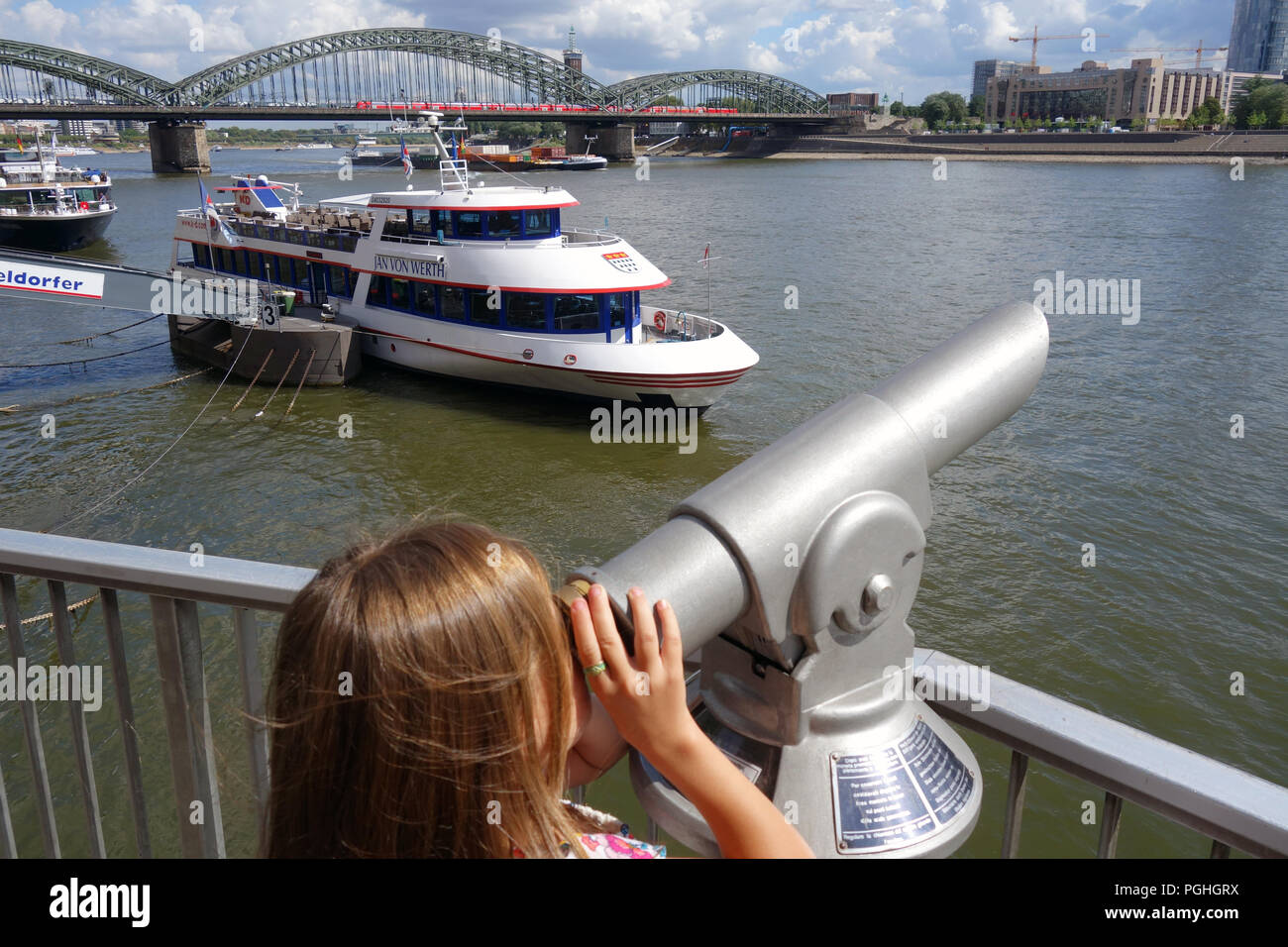 Young girl with long hair looking through a telescope across the Rhine river in Cologne Germany Stock Photo