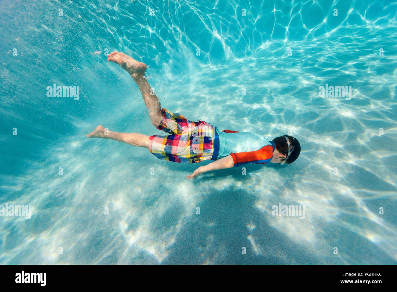 Cute teenage boy swimming underwater in shallow turquoise water at tropical beach Stock Photo