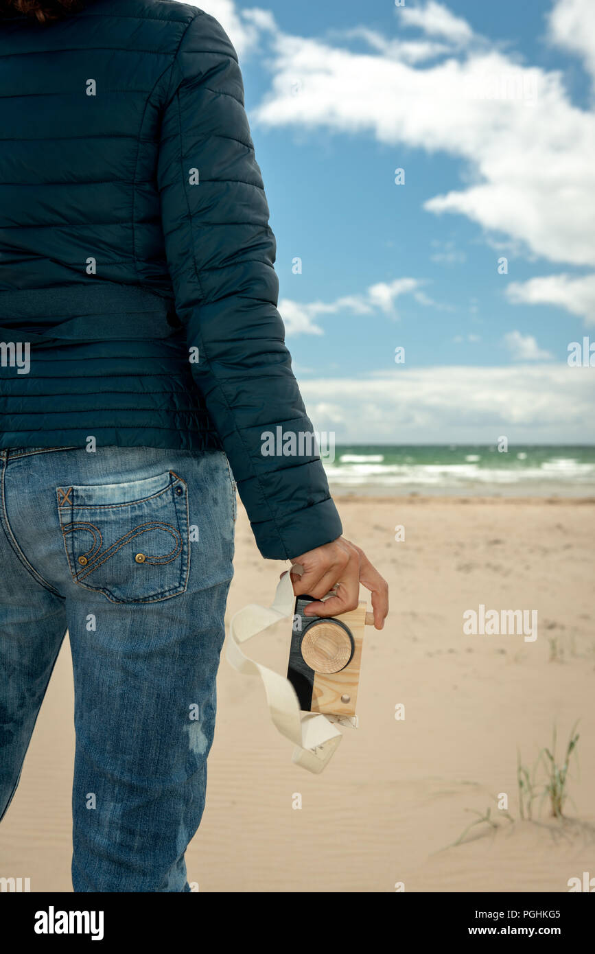 Close-up of woman's hand holding an wooden toy photo camera against sandy beach background.Fun photography concept. Stock Photo