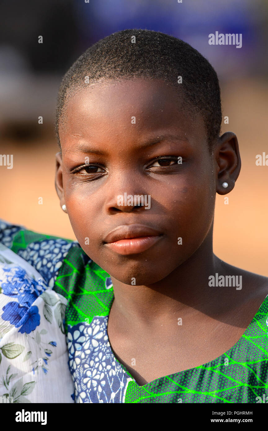 OUIDAH, BENIN - Jan 10, 2017: Unidentified Beninese beautiful girl in colored shirt wears earings at the local market. Benin people suffer of poverty  Stock Photo