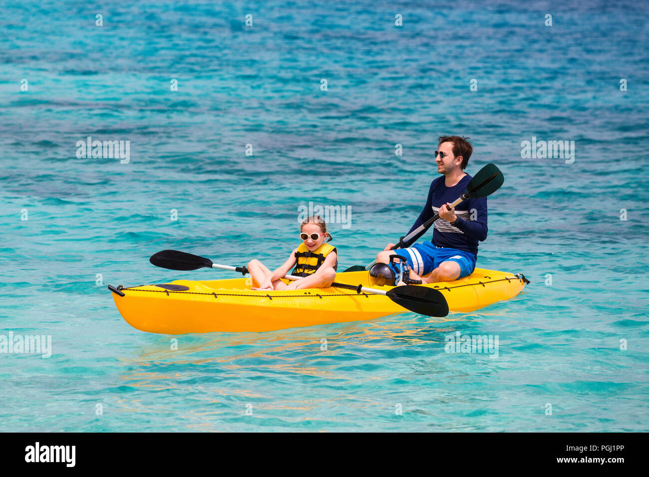 Family of father and daughter paddling on colorful yellow kayaks at tropical ocean water during summer vacation Stock Photo