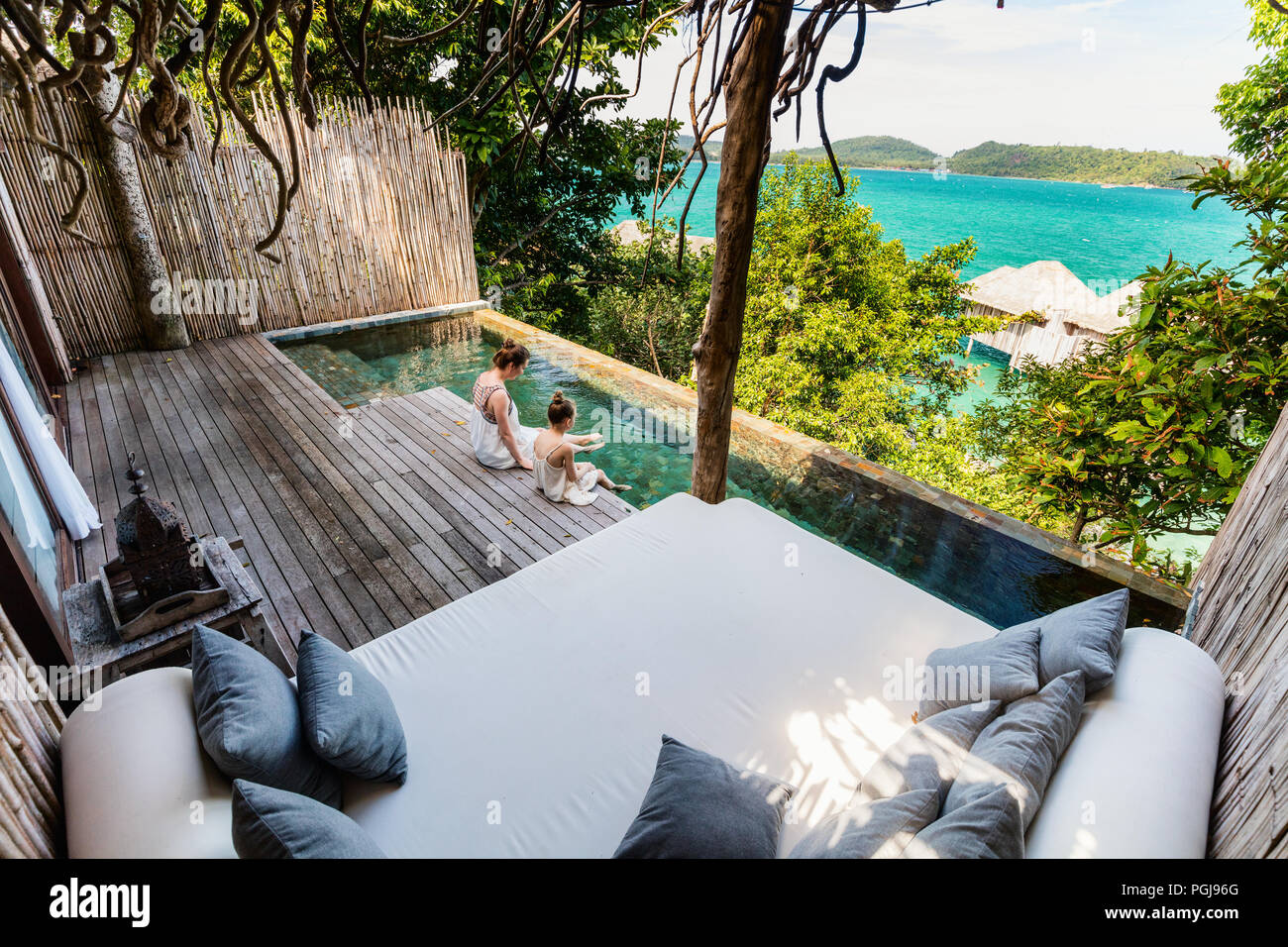 Happy mother and her adorable little daughter outdoors at villa with infinity swimming pool at tropical resort enjoying views over overwater bungalows Stock Photo