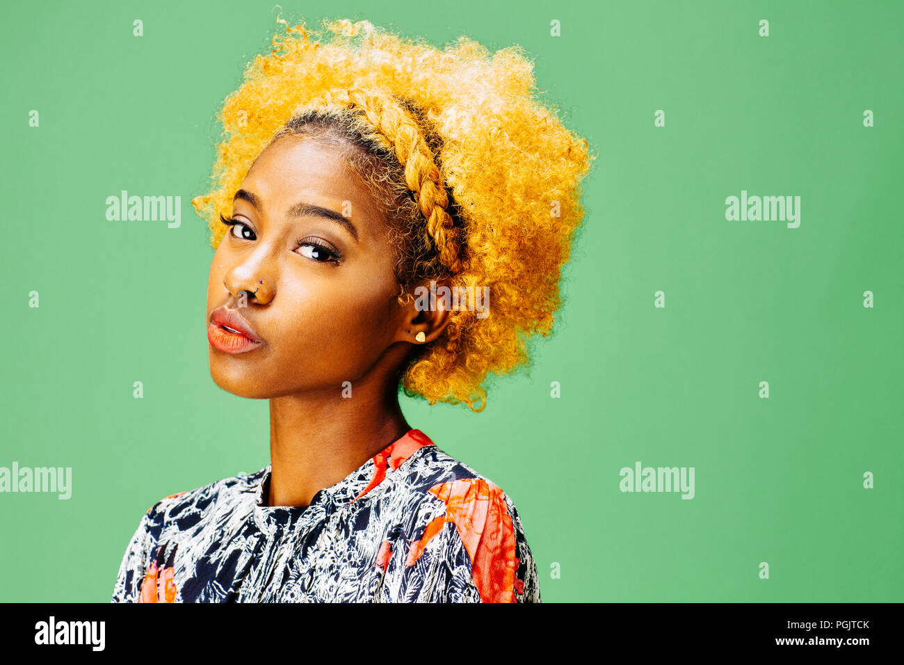 Portrait of a lovely young girl with bleached curly hair, in front of a green background Stock Photo