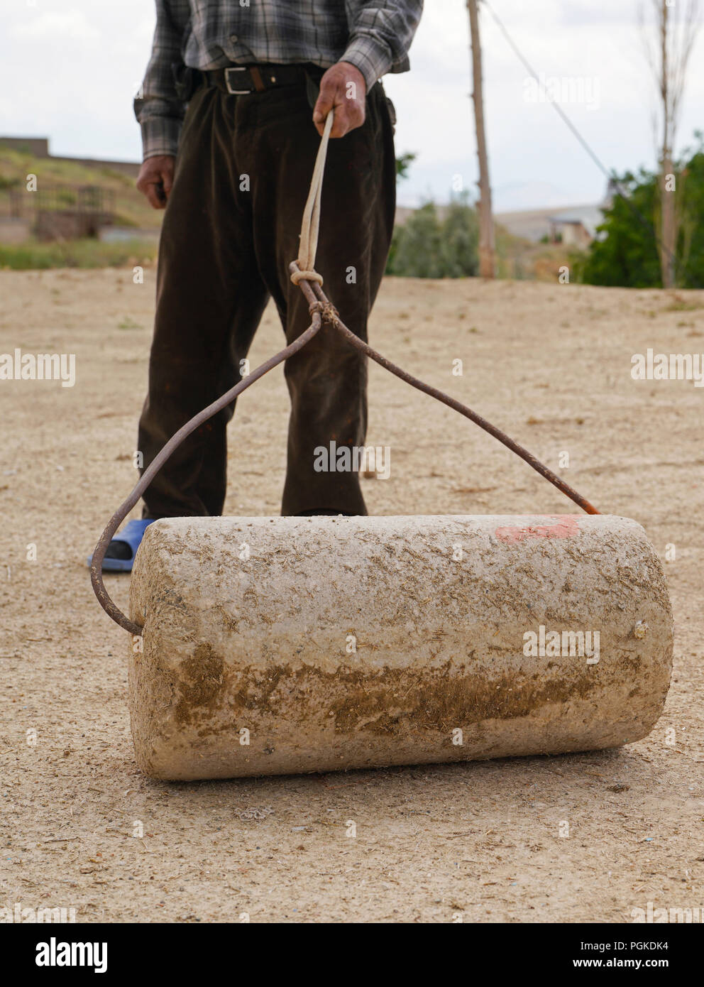 Old man uses stone roller to compress the flat roof of earthsheltered