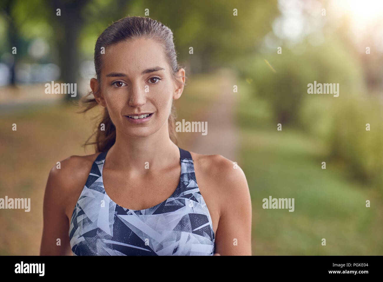 Attractive young woman iin sports attire and a ponytail standing outdoors in a rural park looking pensively at the camera in a close up head and shoul Stock Photo