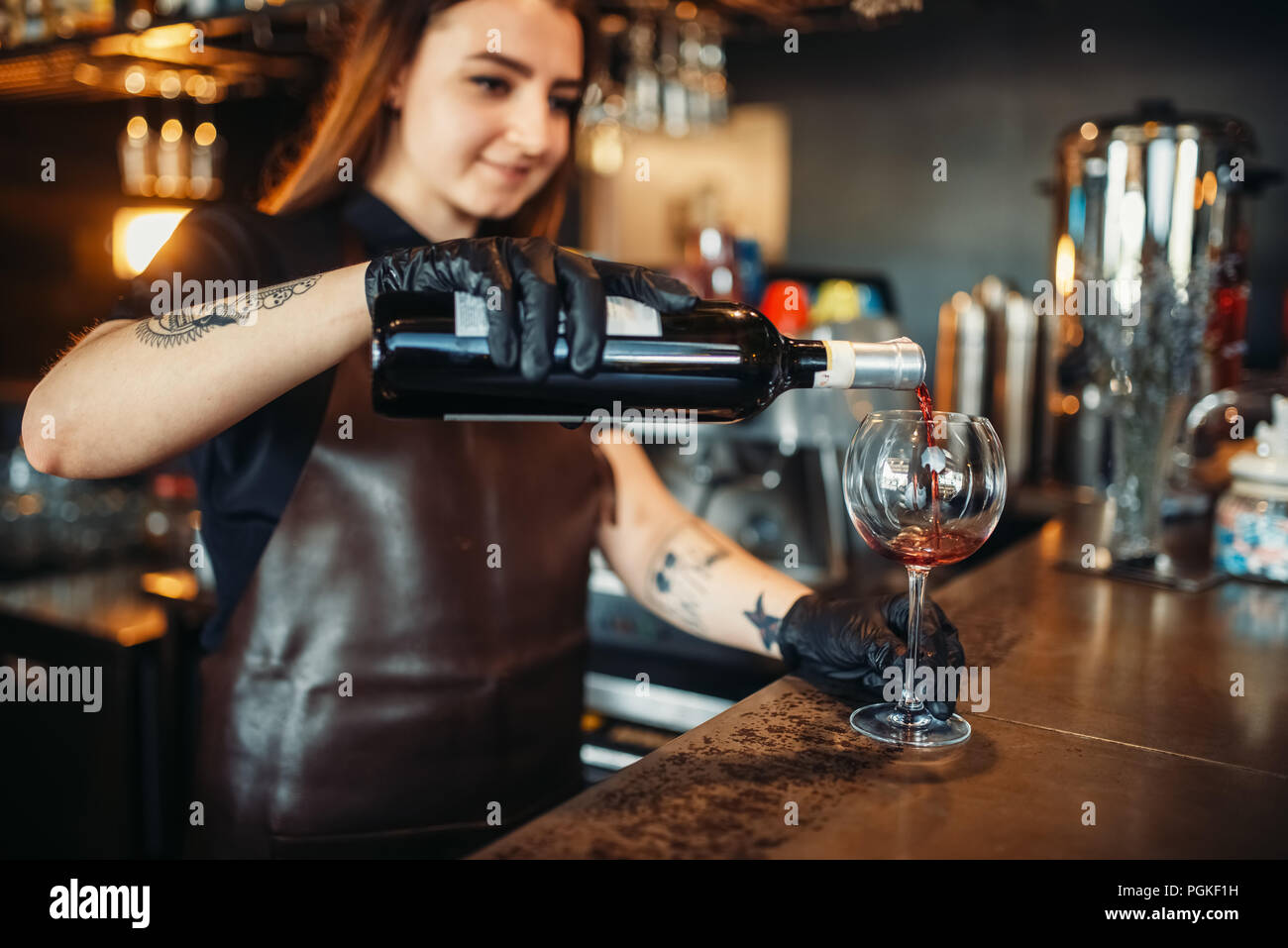 Female barman pours red wine into a glass. Woman bartender working at the bar counter in pub. Barkeeper occupation Stock Photo